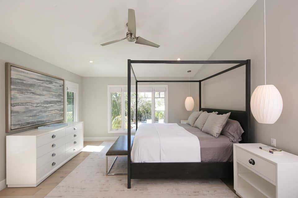 Modern bedroom with a black canopy bed, white dresser, and light gray walls.