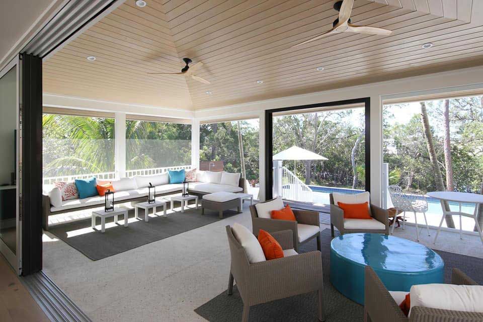 Spacious outdoor living area with couches, chairs, a pool, and retractable screens. Beige and white tones, teal accents.