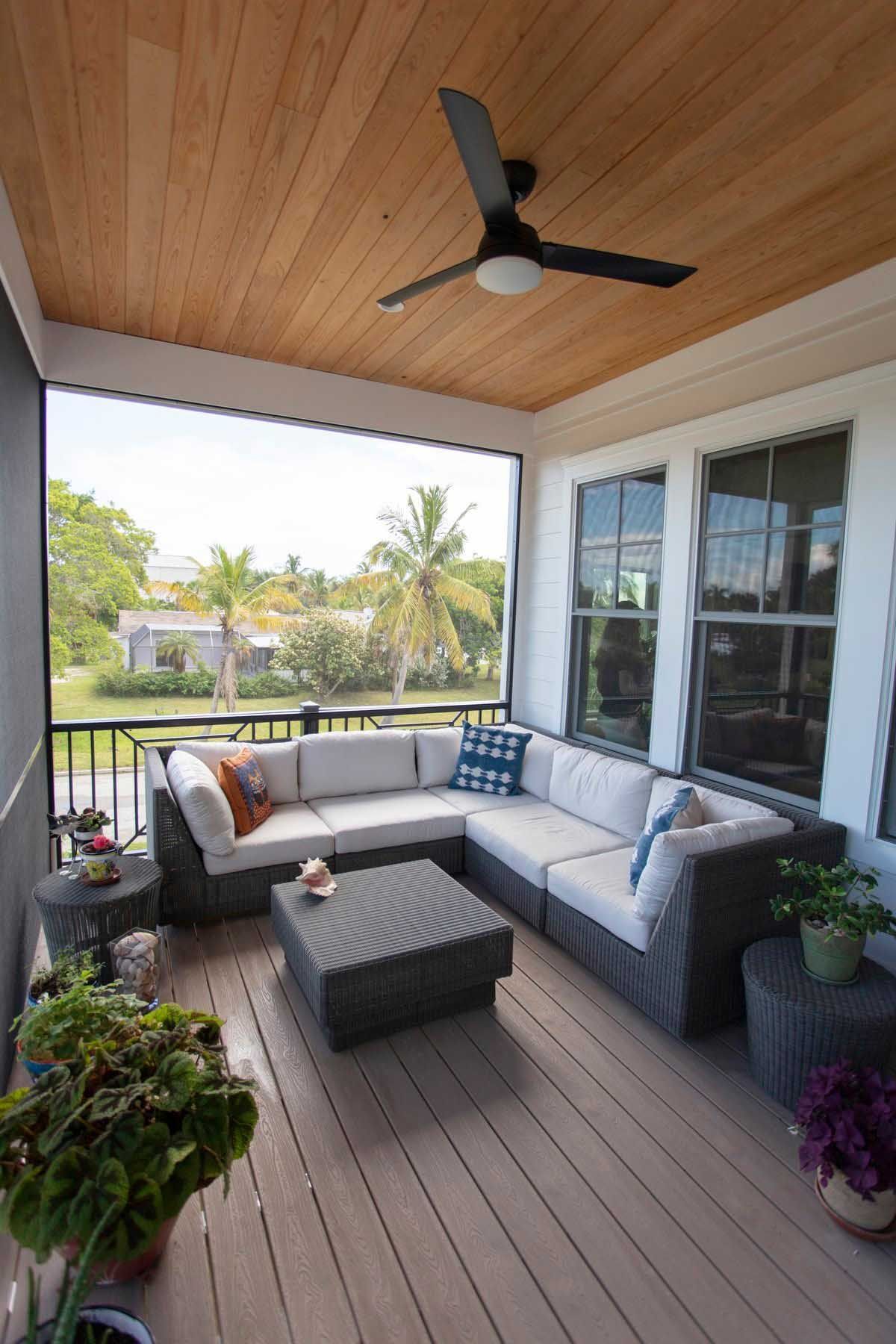 Outdoor screened-in porch with sectional sofa, coffee table, and ceiling fan; wooden ceiling and flooring.
