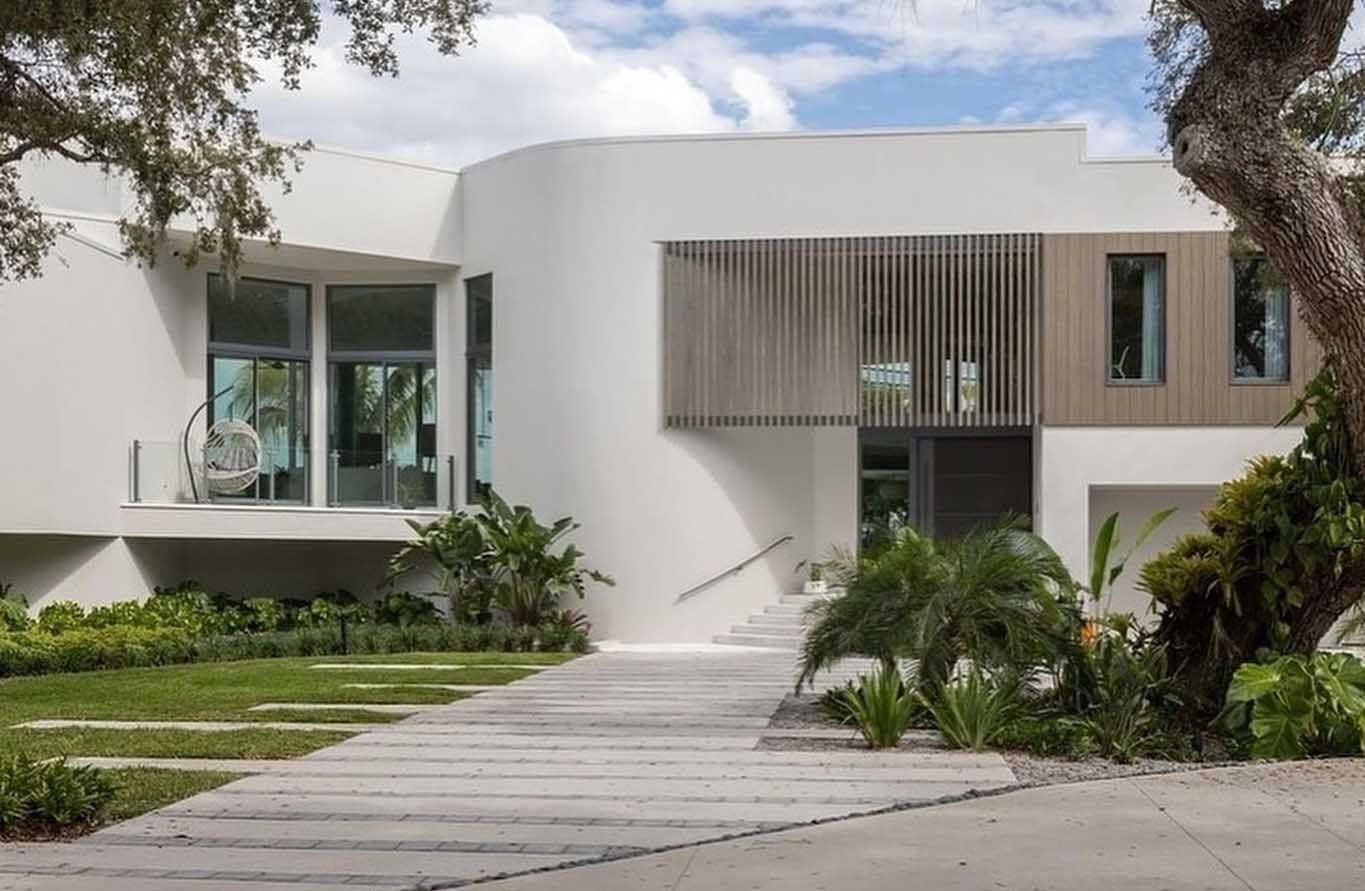 Modern white house with gray walkway, green landscaping, and wooden accents.
