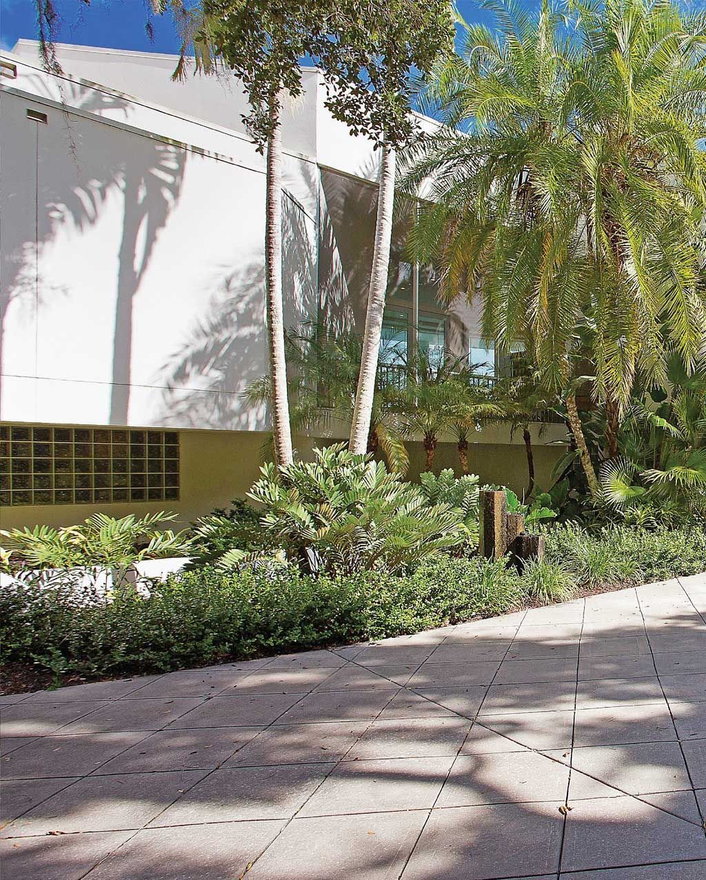 A building with a sidewalk and lush landscaping, including trees and greenery.