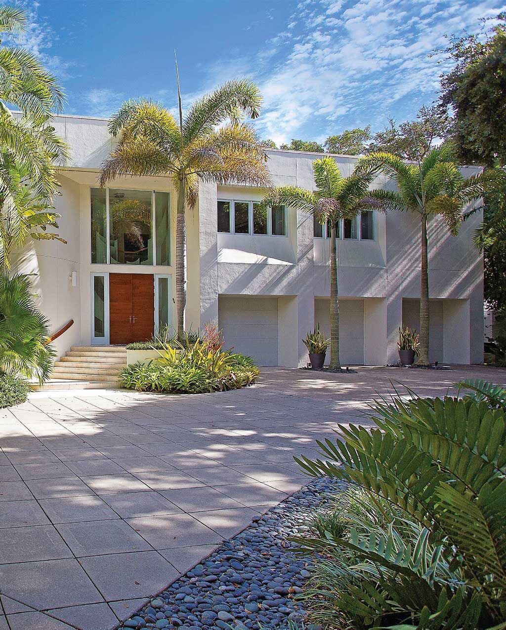 White modern home with a red door, palm trees, and a paved driveway.