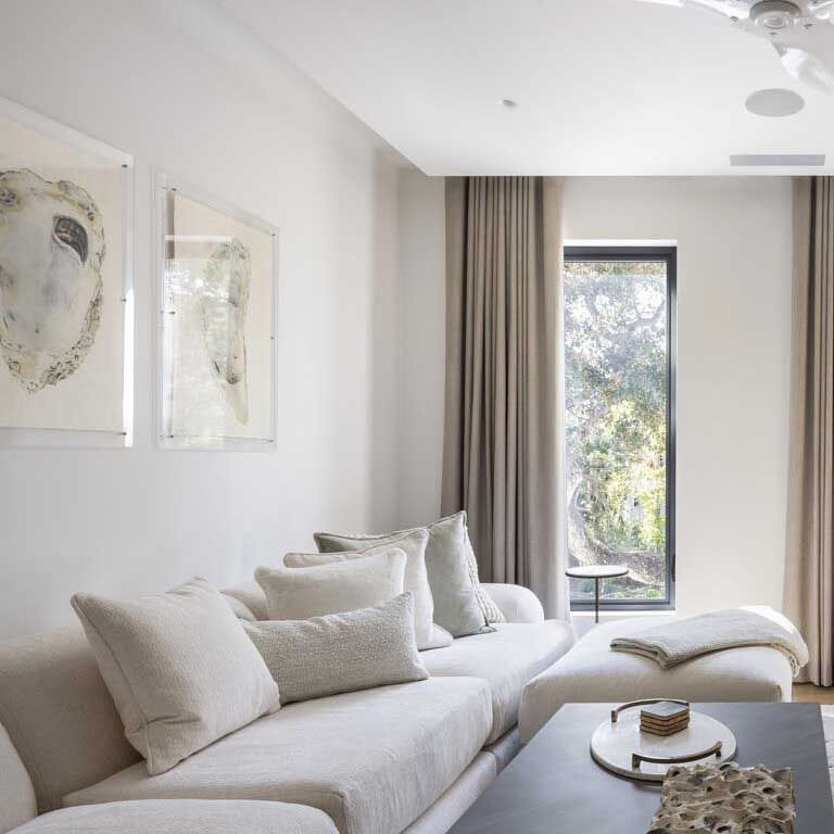 White living room with a cream sofa, framed art, and a window with neutral drapes.