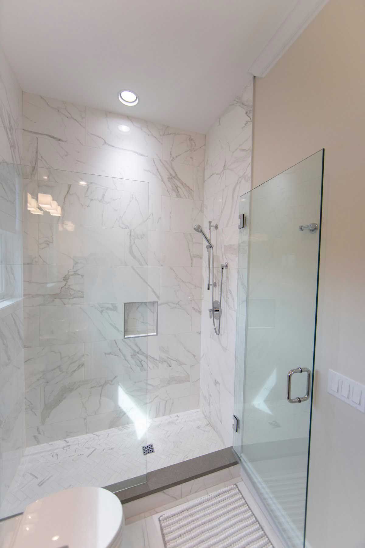 A modern shower with marble walls, glass door, and chrome fixtures.