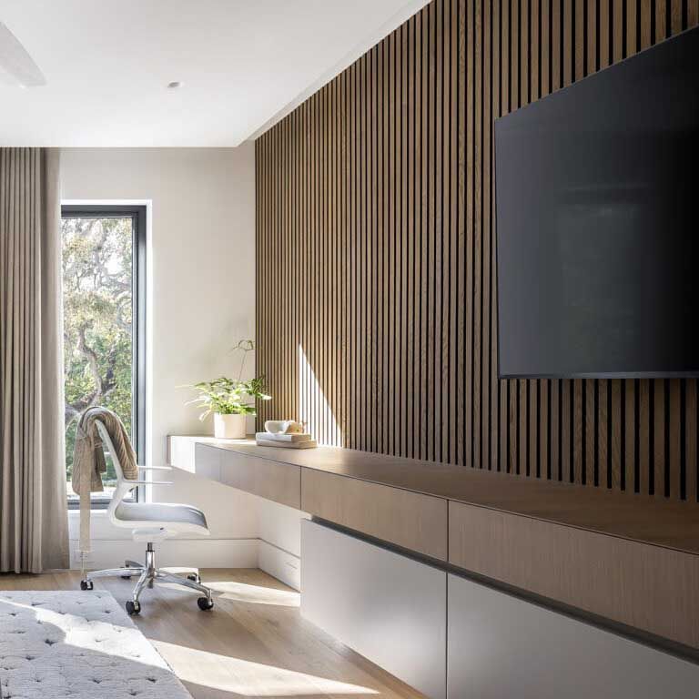 Modern home office with wood slat wall, desk, TV, and window with natural light.