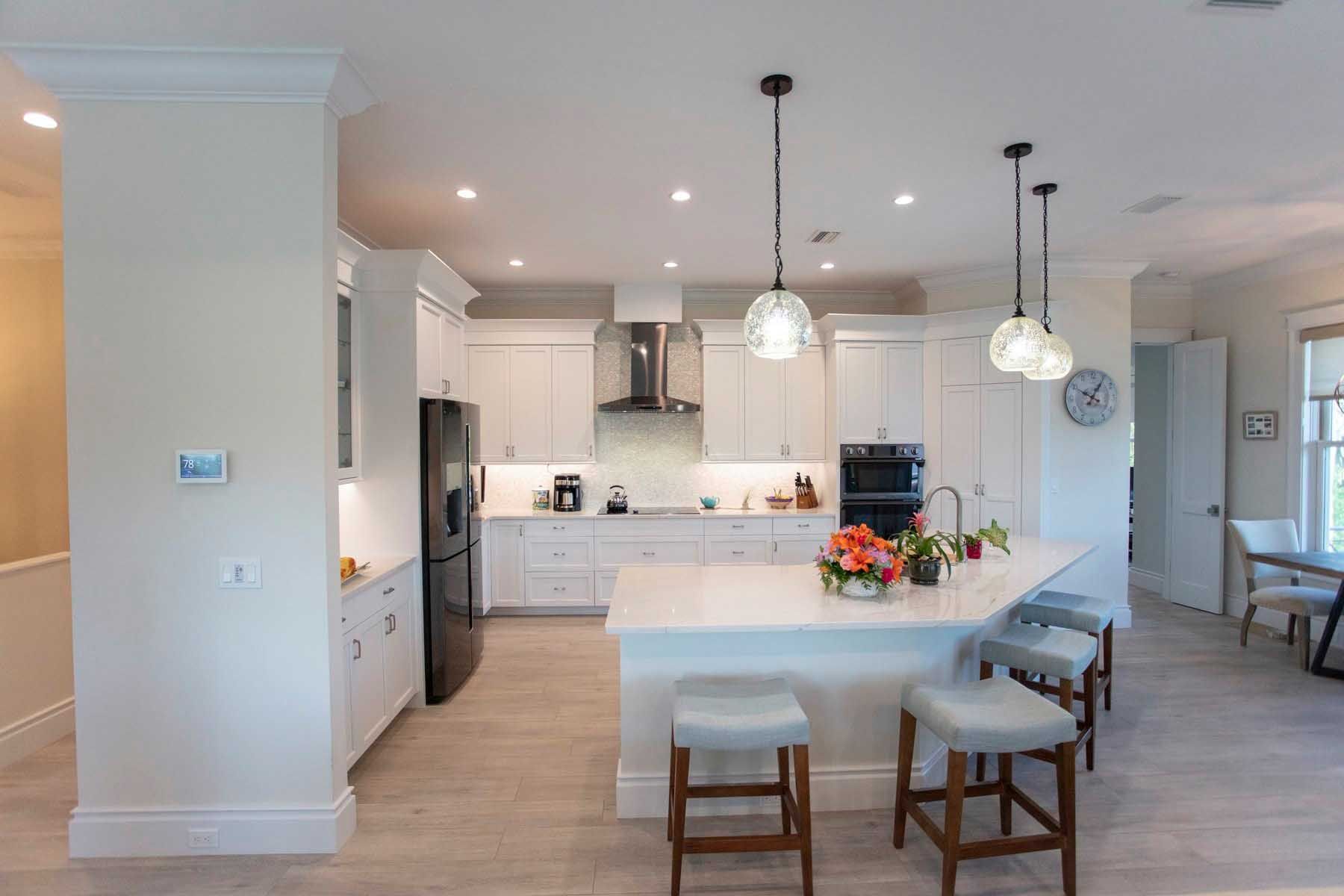 Modern white kitchen with island, black appliances, pendant lights, and bar stools.