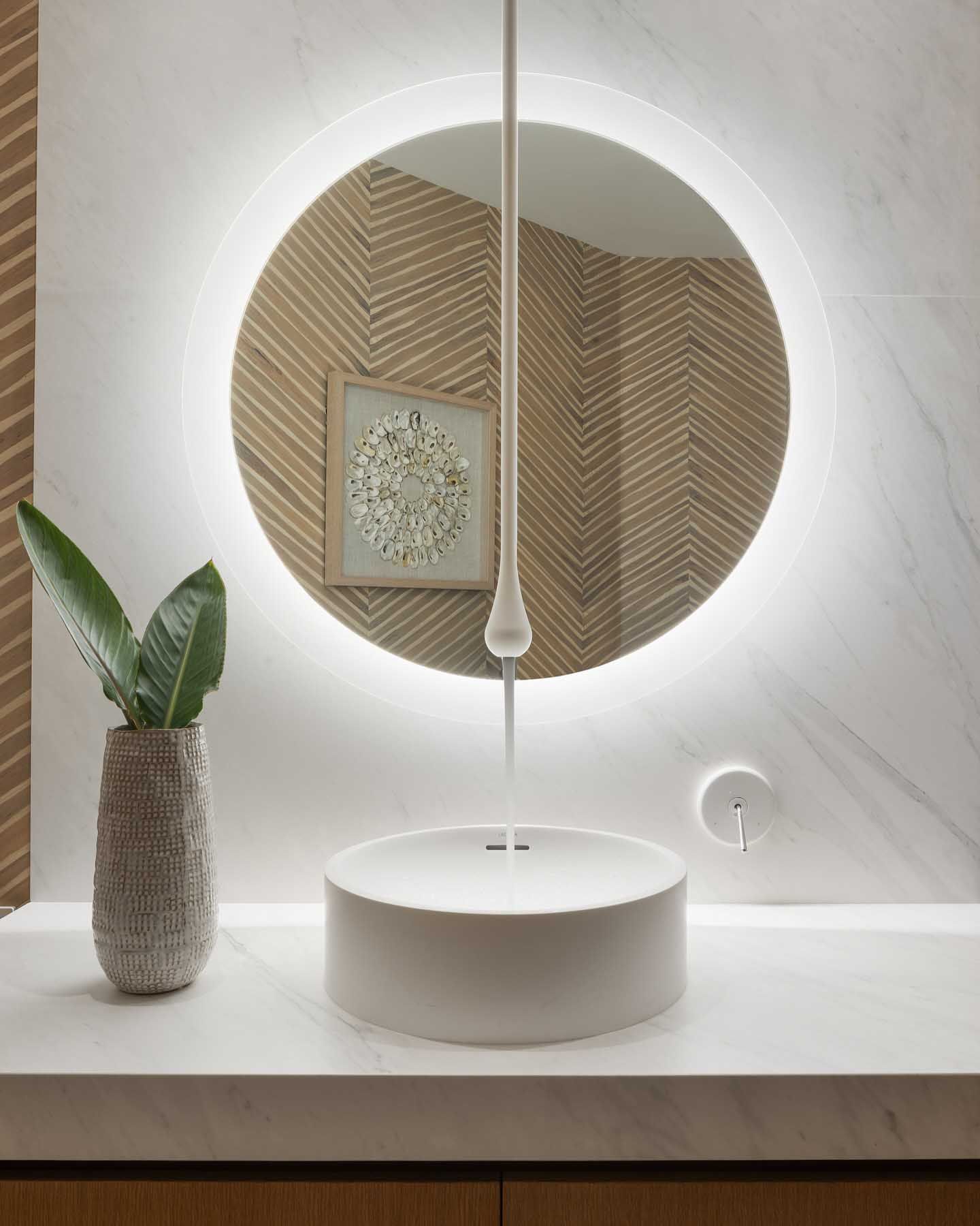 Modern bathroom with round mirror, circular sink, and plant in vase.