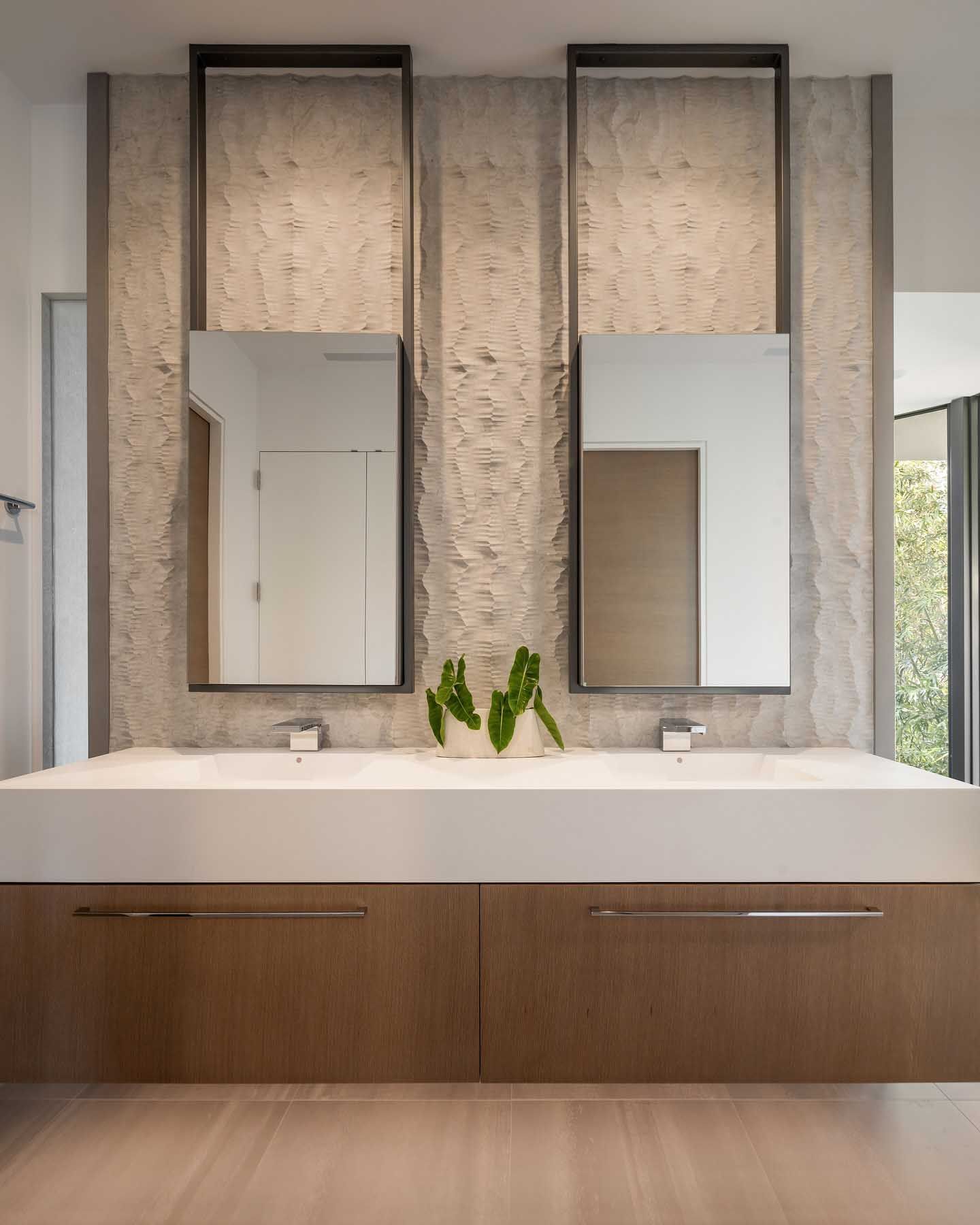 Modern bathroom with dual sinks, stone wall, framed mirrors, and wood cabinetry.