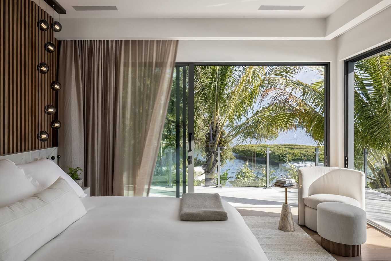 Bedroom with bed, chair, and large window overlooking water and trees.