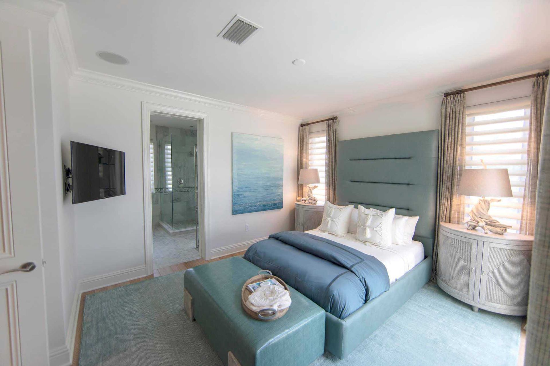 A bedroom with teal accents. Bed with headboard, two nightstands, a bench, and a bathroom.