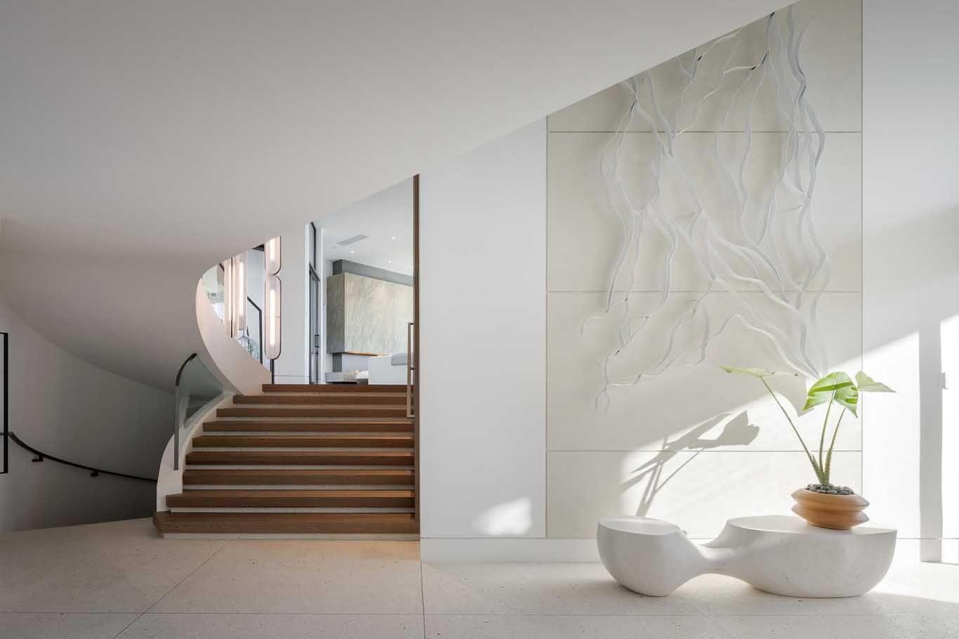 Modern white entry hall with wooden stairs, sculpture, and wall art.