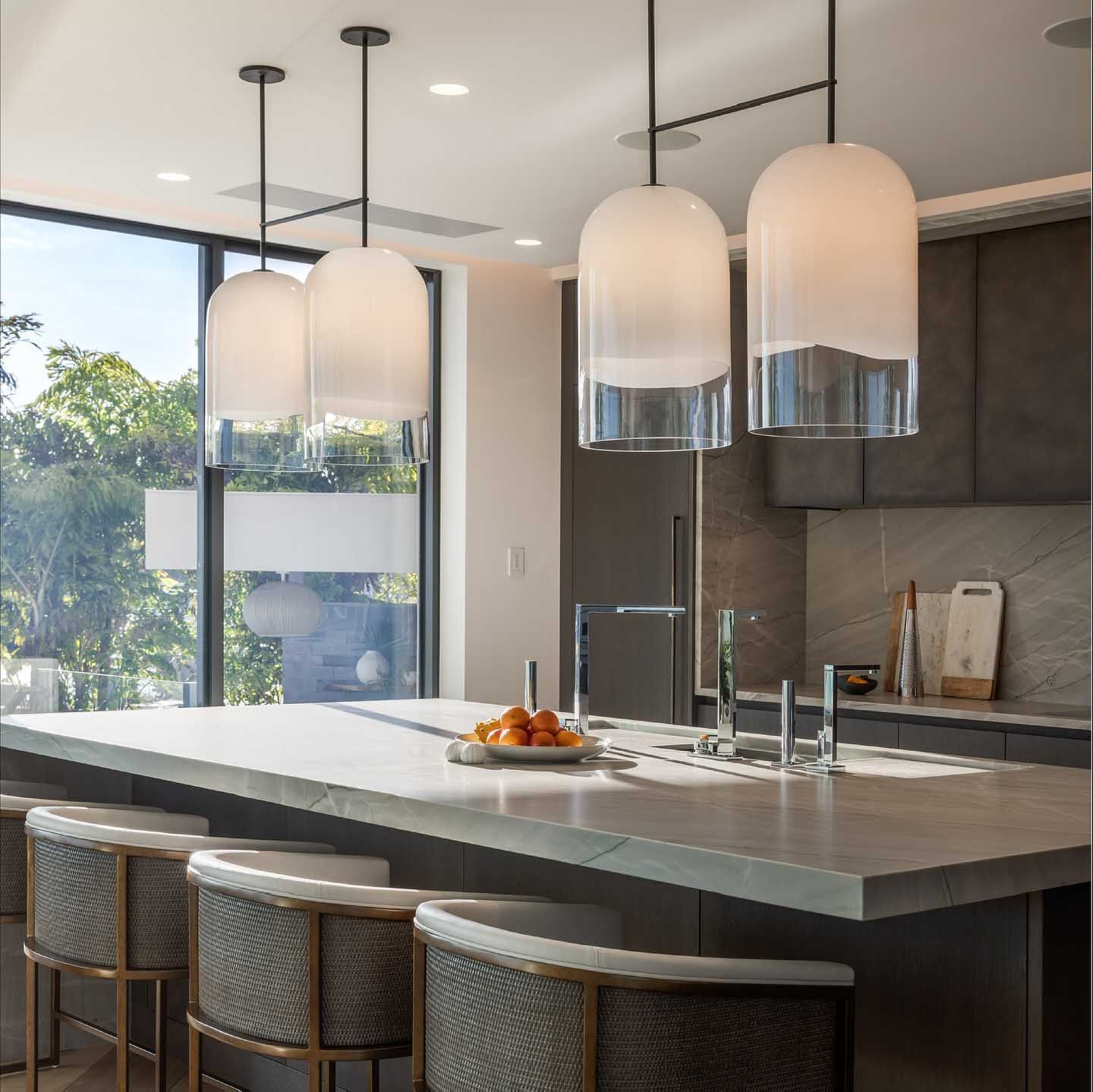 Kitchen with pendant lights over a countertop with bar stools, window, and fruit on a plate.