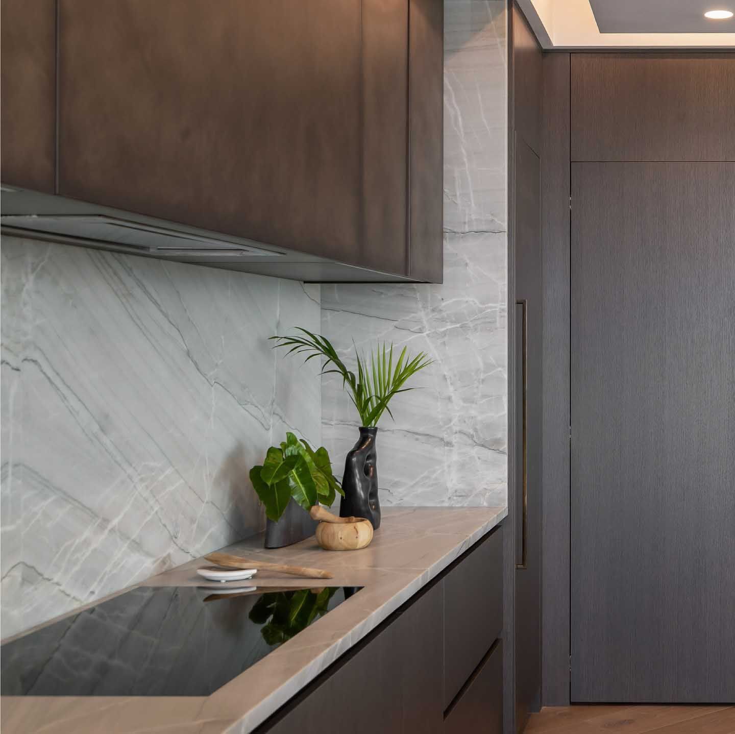 Modern kitchen with gray cabinets, marble backsplash, cooktop, and decorative plants.