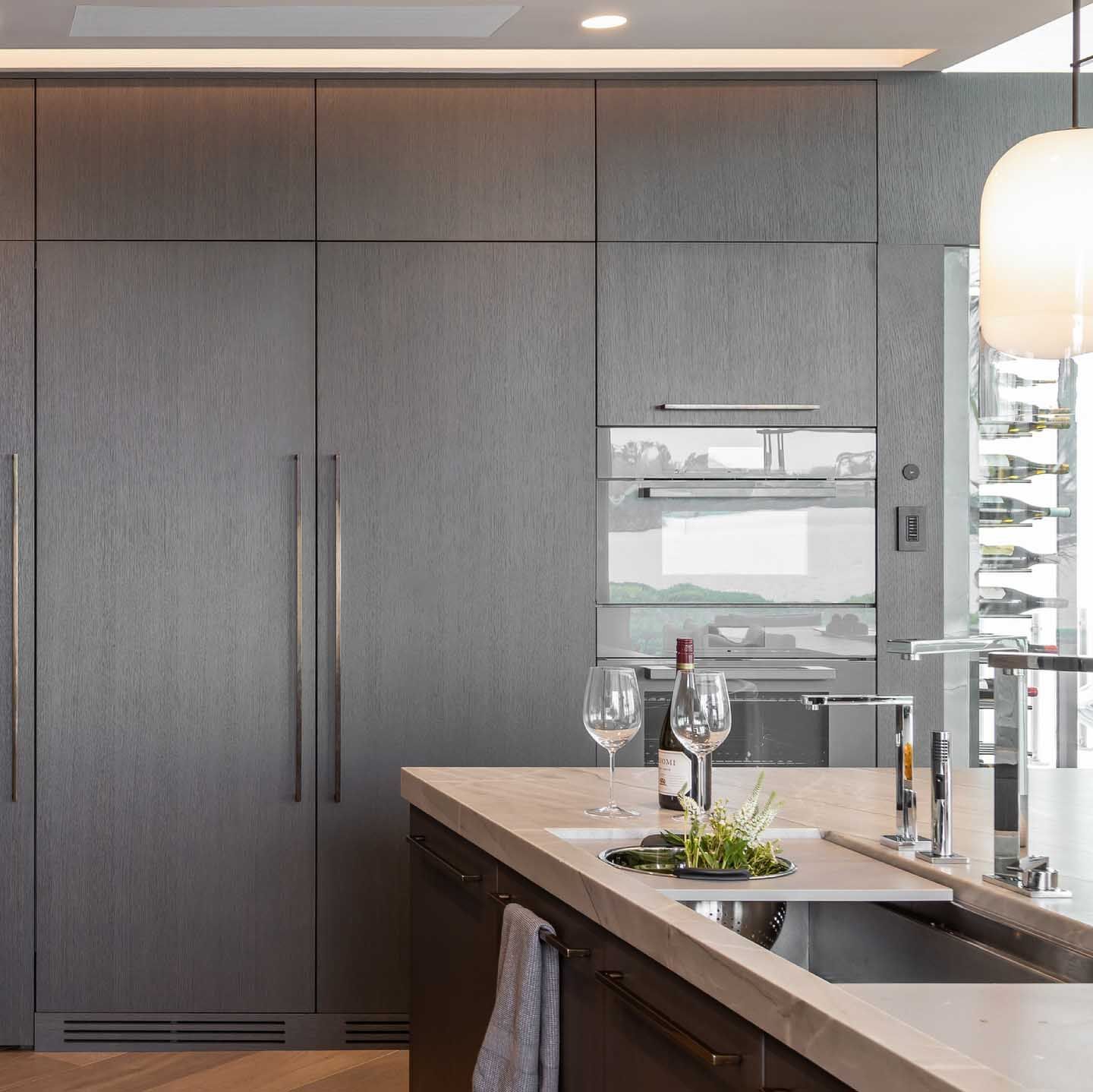 Modern kitchen with dark wood cabinets, built-in oven, and a kitchen island with a sink and glassware.