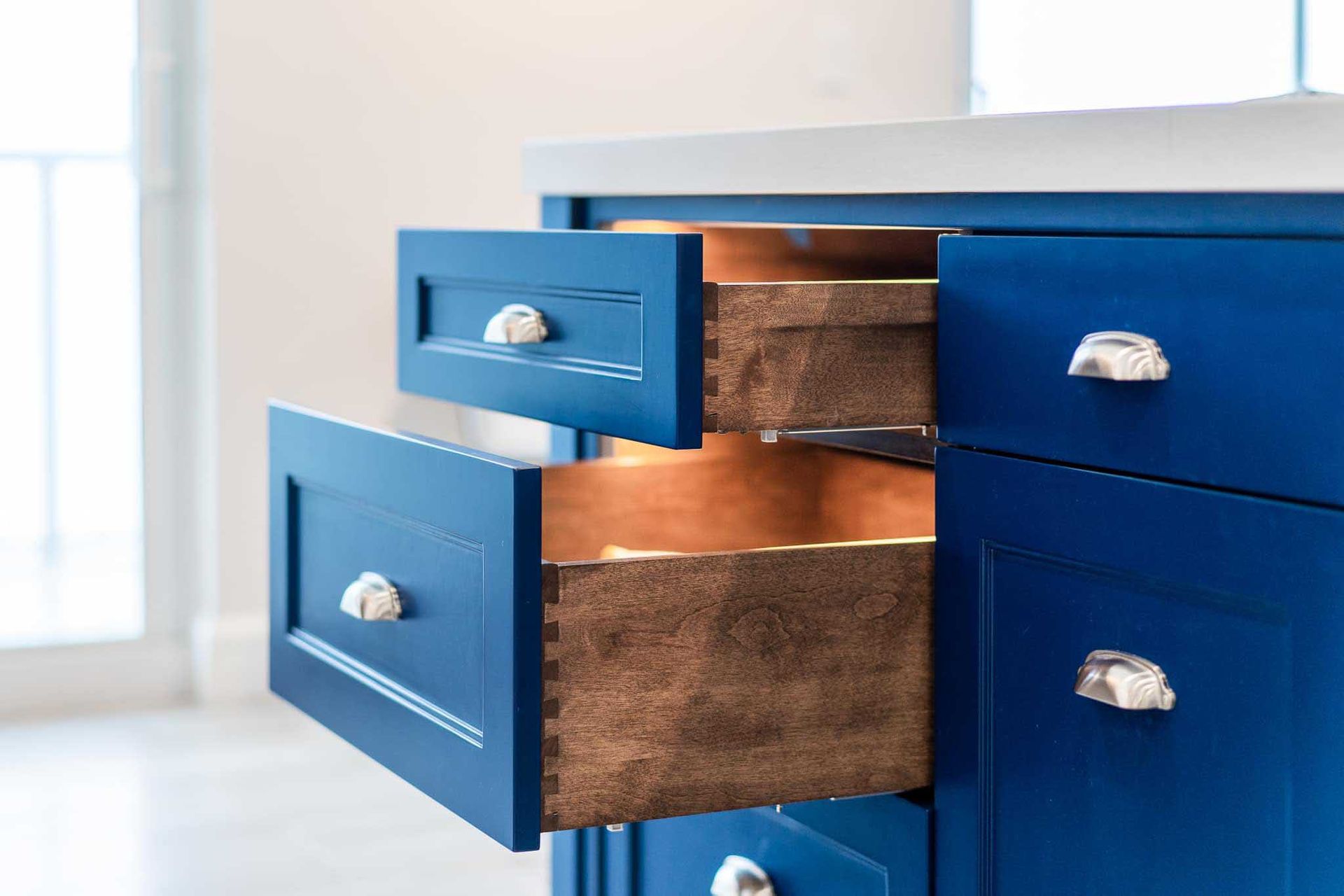 Blue kitchen cabinets with open drawers, revealing wooden interiors and silver handles.