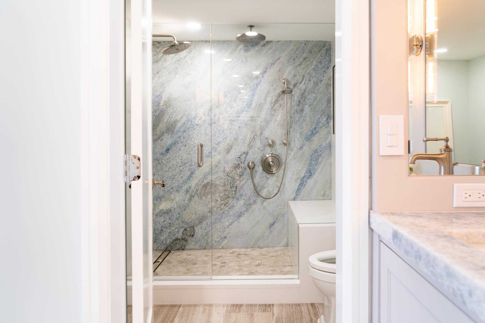 Bathroom interior with a blue marble-tiled shower, glass door, white walls, and a toilet.