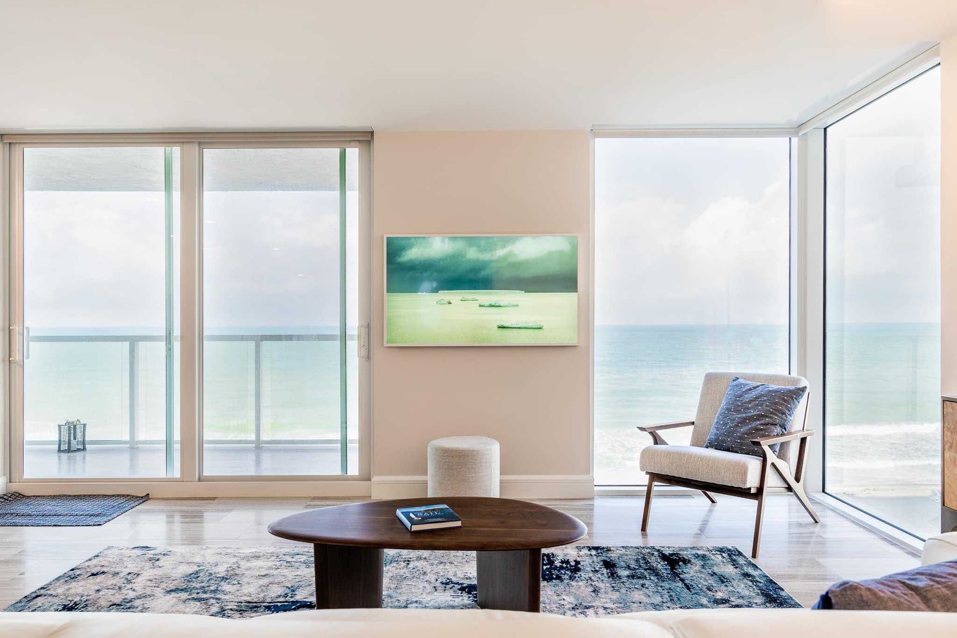 Living room with ocean view, large windows, TV, chair, and coffee table.