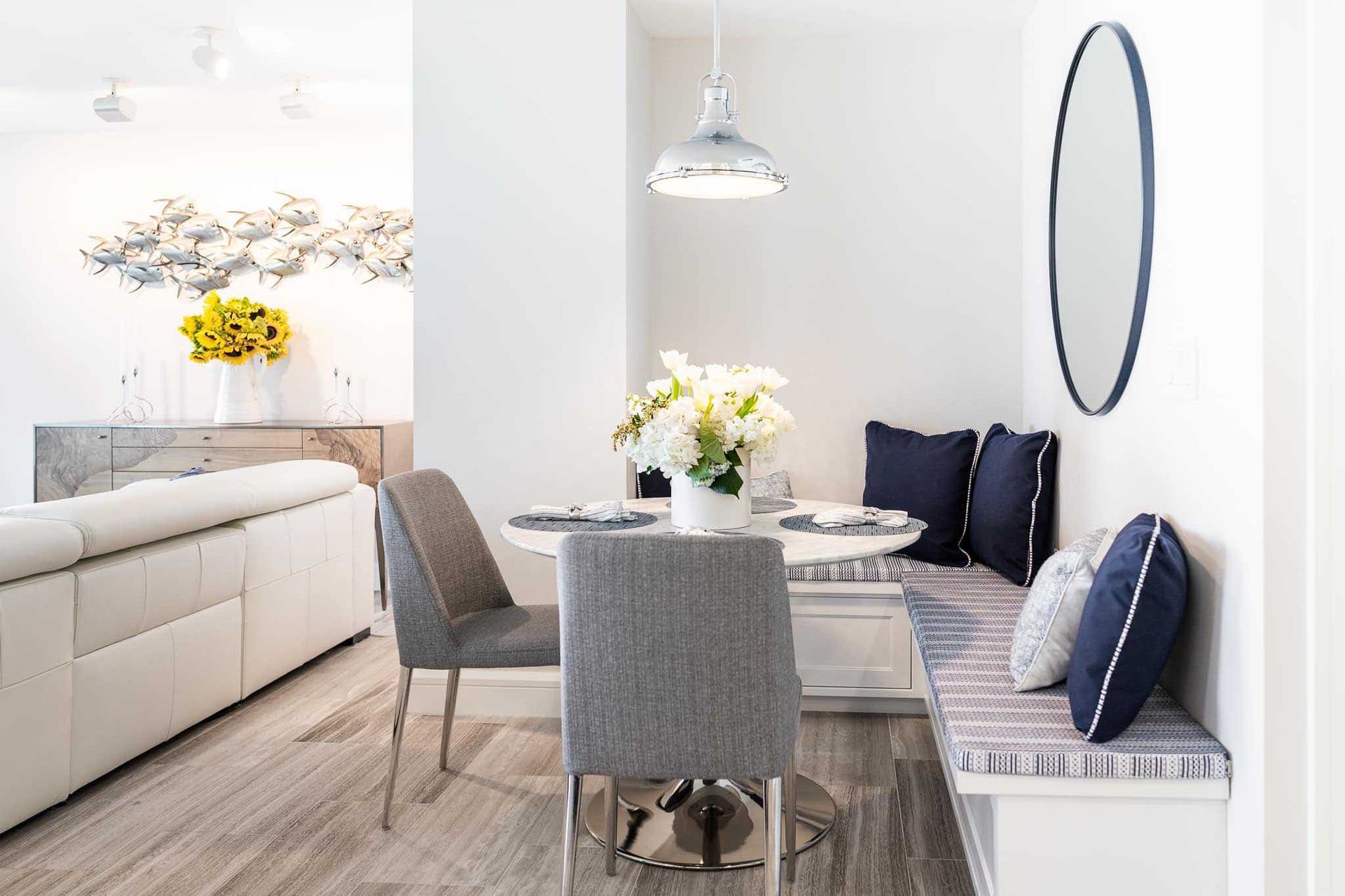 Dining nook with round table, built-in bench, gray chairs, white walls, and a hanging light.