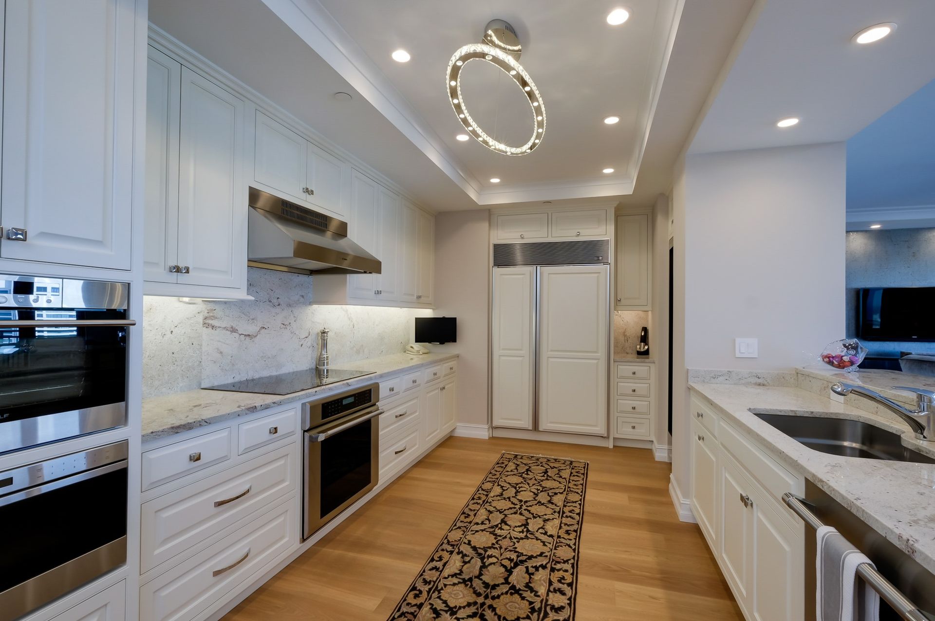 Modern white kitchen with stainless steel appliances, granite countertops, and light wood flooring.