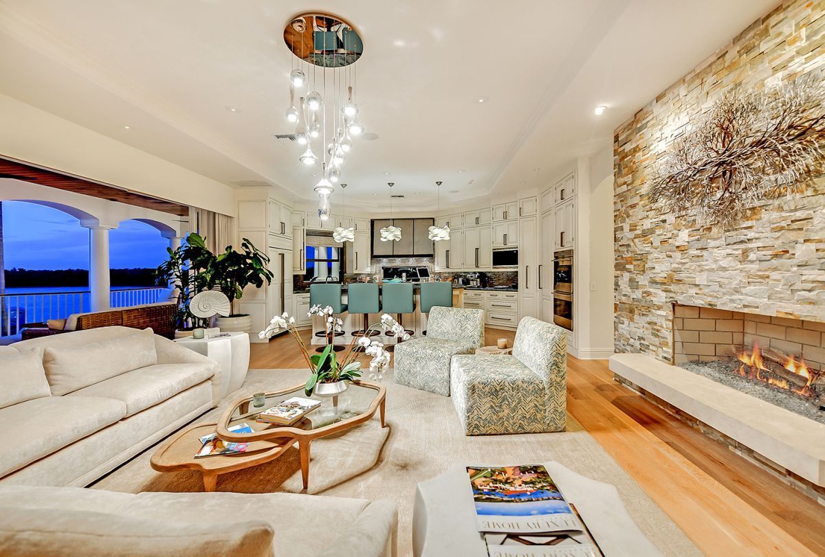 Luxurious living room with fireplace, white couches, and bar seating overlooking water at dusk.
