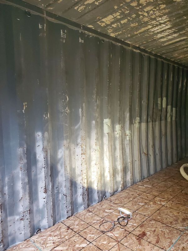 Interior of a shipping container with gray walls and a wood floor; some equipment is on the floor.