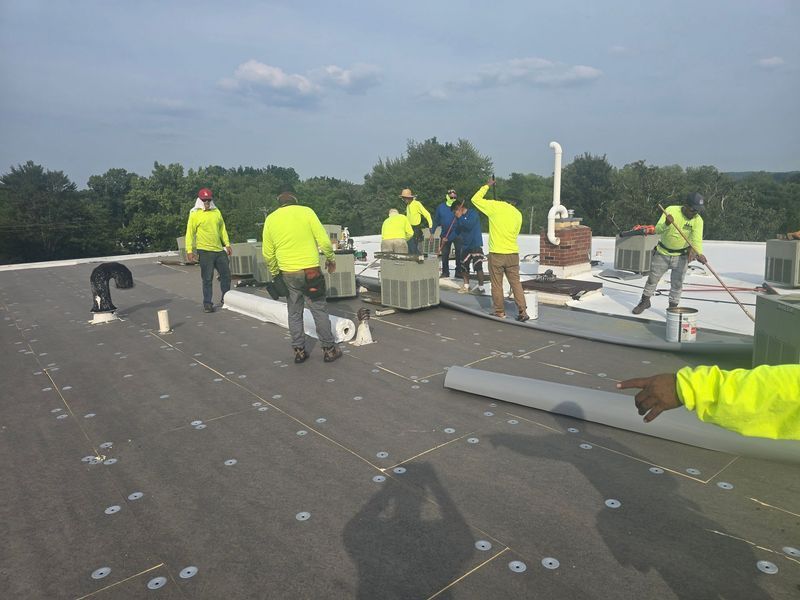 Construction workers in yellow vests on a flat roof, working near equipment and markings.
