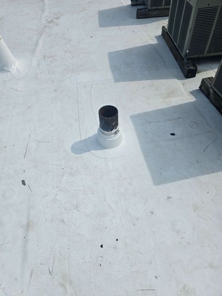 Black pipe and white collar on a white commercial roof. Air conditioning units are in the background.