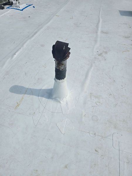 Black pipe vent sealed to a white roof. Shadow and markings visible around the base.