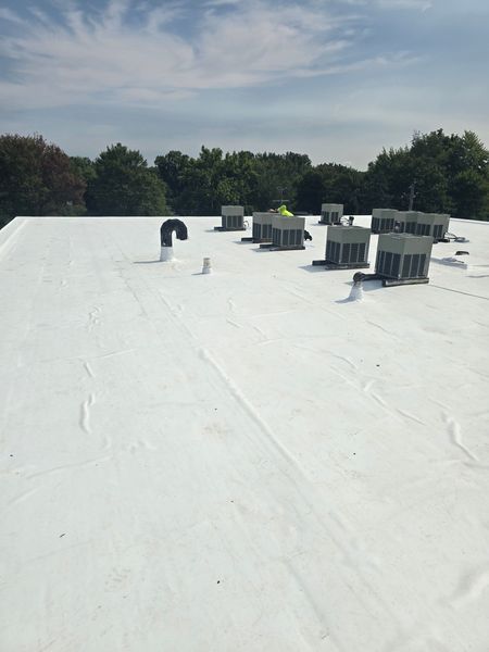 White commercial roof with HVAC units and vents, trees, and sky.