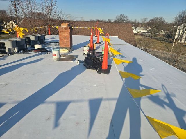 Rooftop with safety cones, yellow flags, and equipment; a chimney stands in the center.