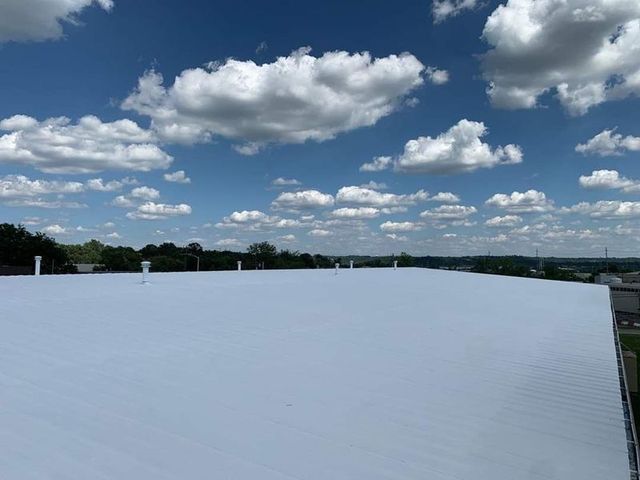 White roof of a building under a blue sky with fluffy white clouds.