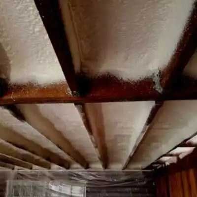 Wooden ceiling beams with spray foam insulation, the area appears to be unfinished construction.