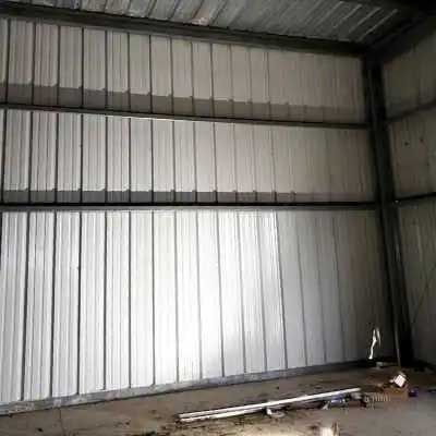 Interior view of a metal building with vertical corrugated panels, three tiers high. The floor is concrete.