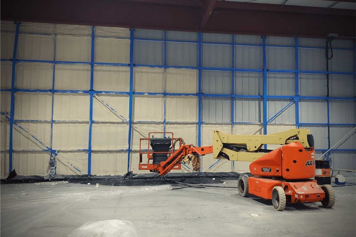 Construction site with orange lifts and a building with blue-framed panels.