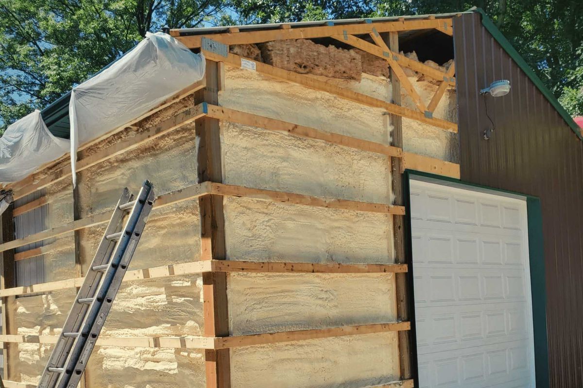 Building exterior under construction; wood frame with spray foam insulation. A ladder leans against the structure.