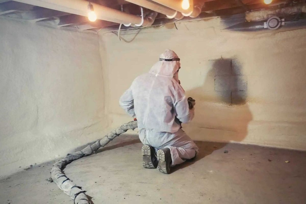 Person in protective suit spraying insulation in a basement.