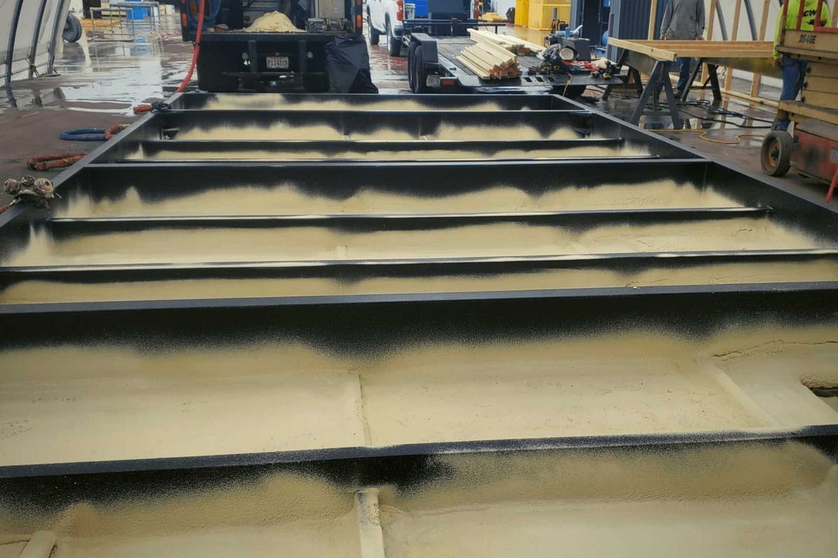 Steel frame coated with tan material, possibly insulation, inside a factory setting.