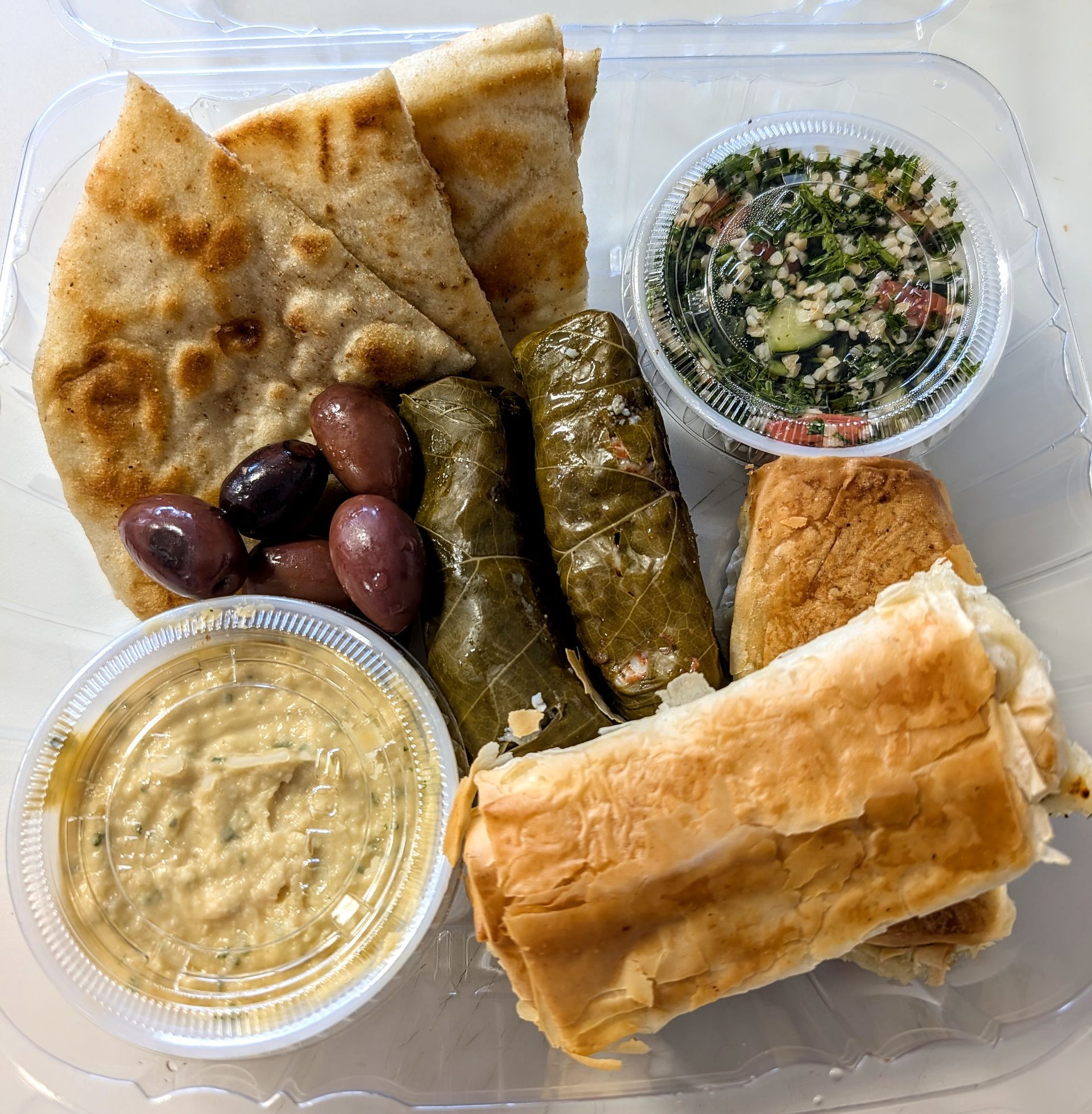 A plastic container filled with bread , olives , dips and pita bread.