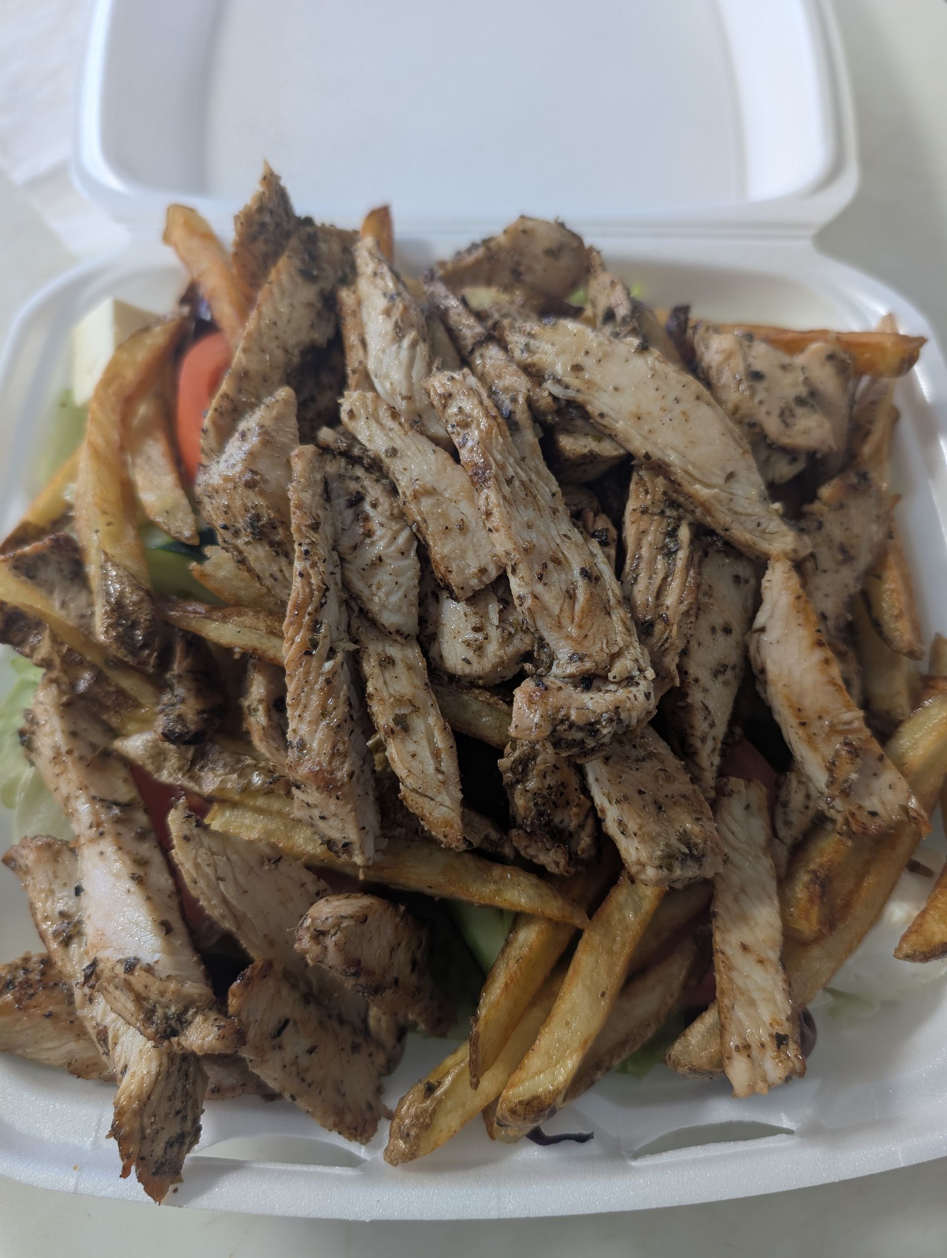 A styrofoam container filled with chicken and french fries.