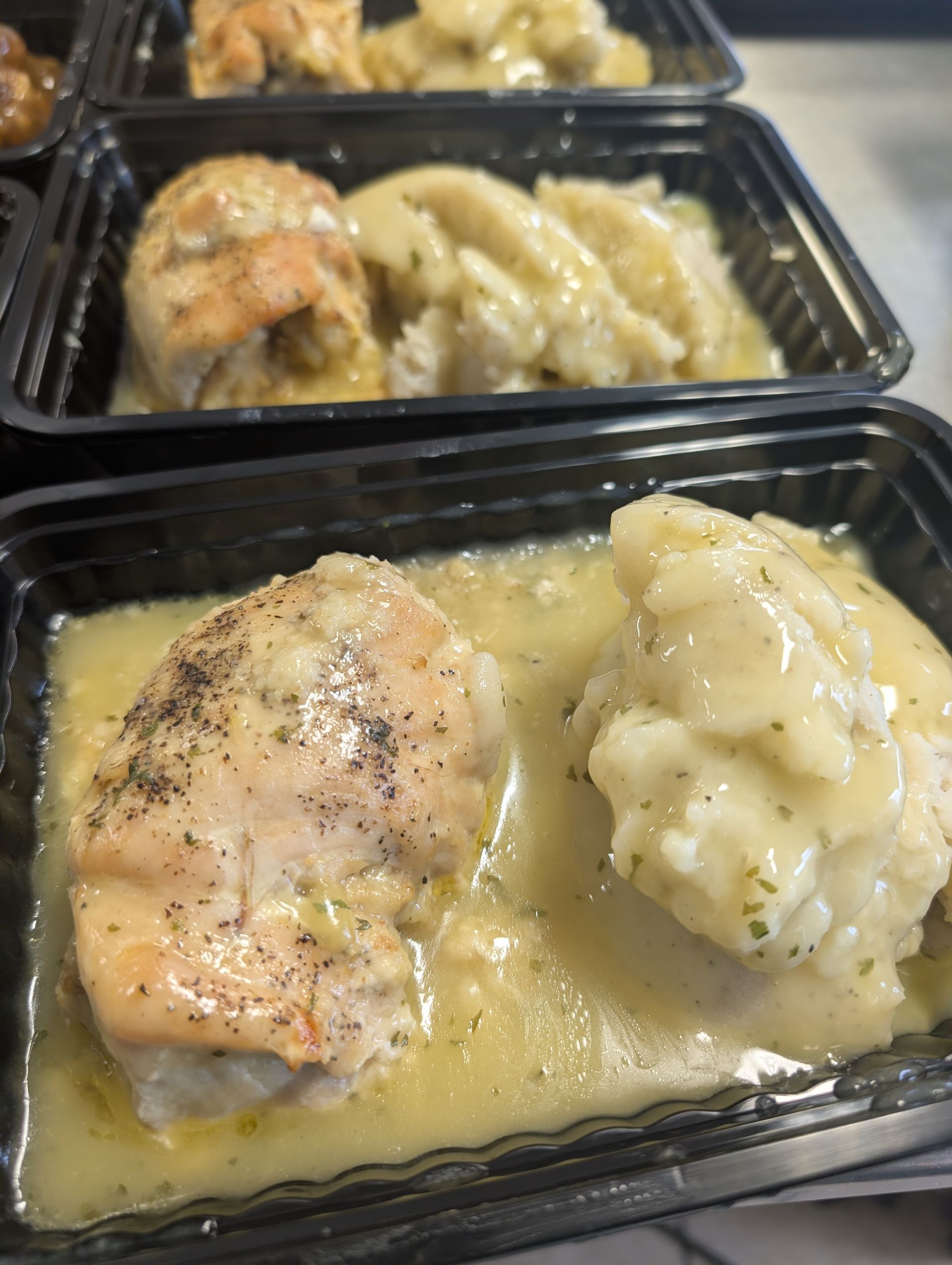 A close up of a tray of food with chicken and mashed potatoes