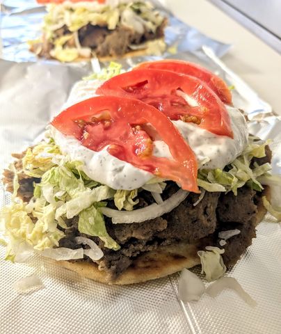 A close up of a gyro sandwich with tomatoes , lettuce and ranch dressing on a napkin.