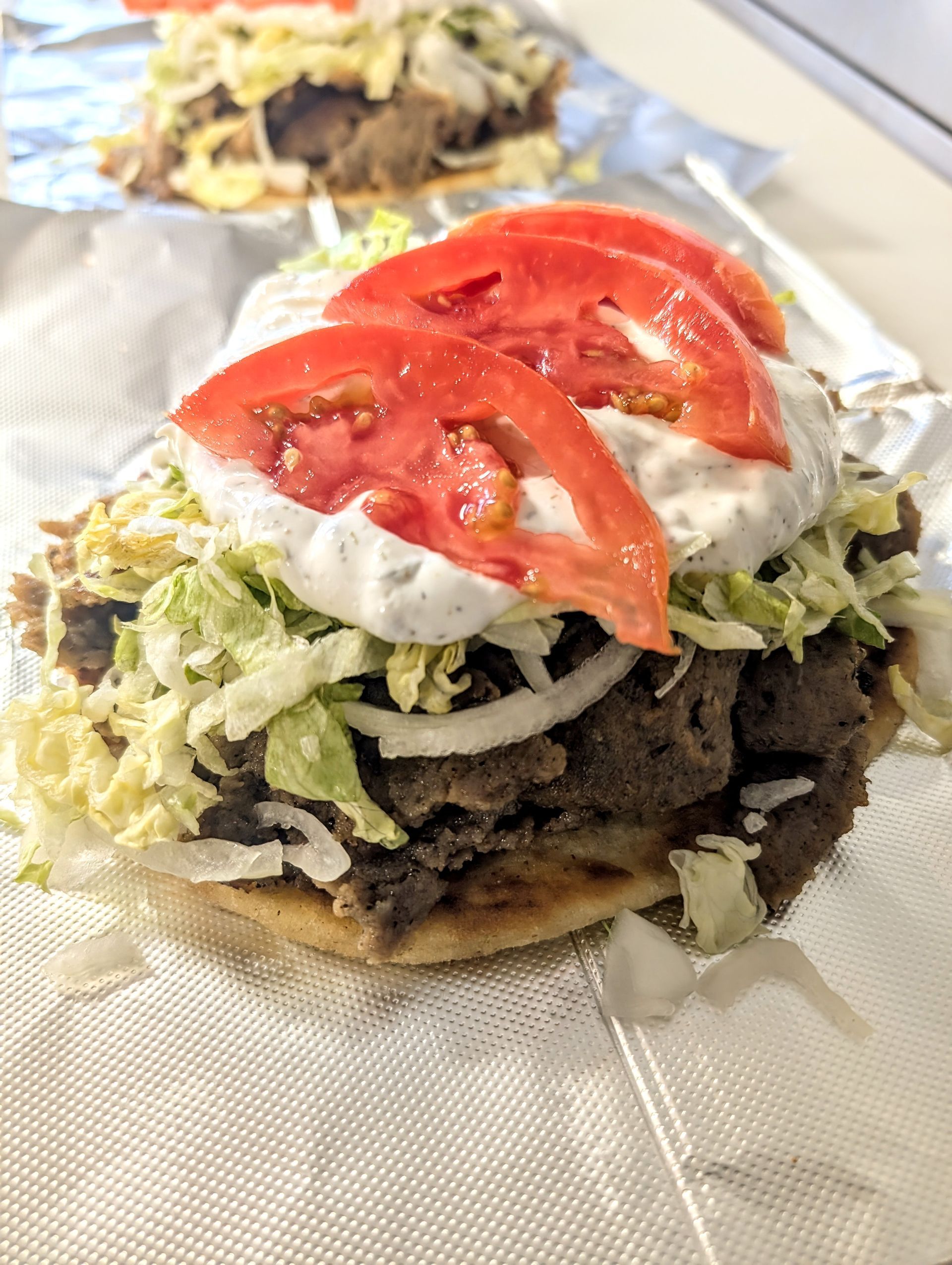 A close up of a gyro sandwich with tomatoes , lettuce and ranch dressing on a napkin.