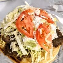 A close up of a gyro sandwich with lettuce , tomatoes , and ranch dressing.