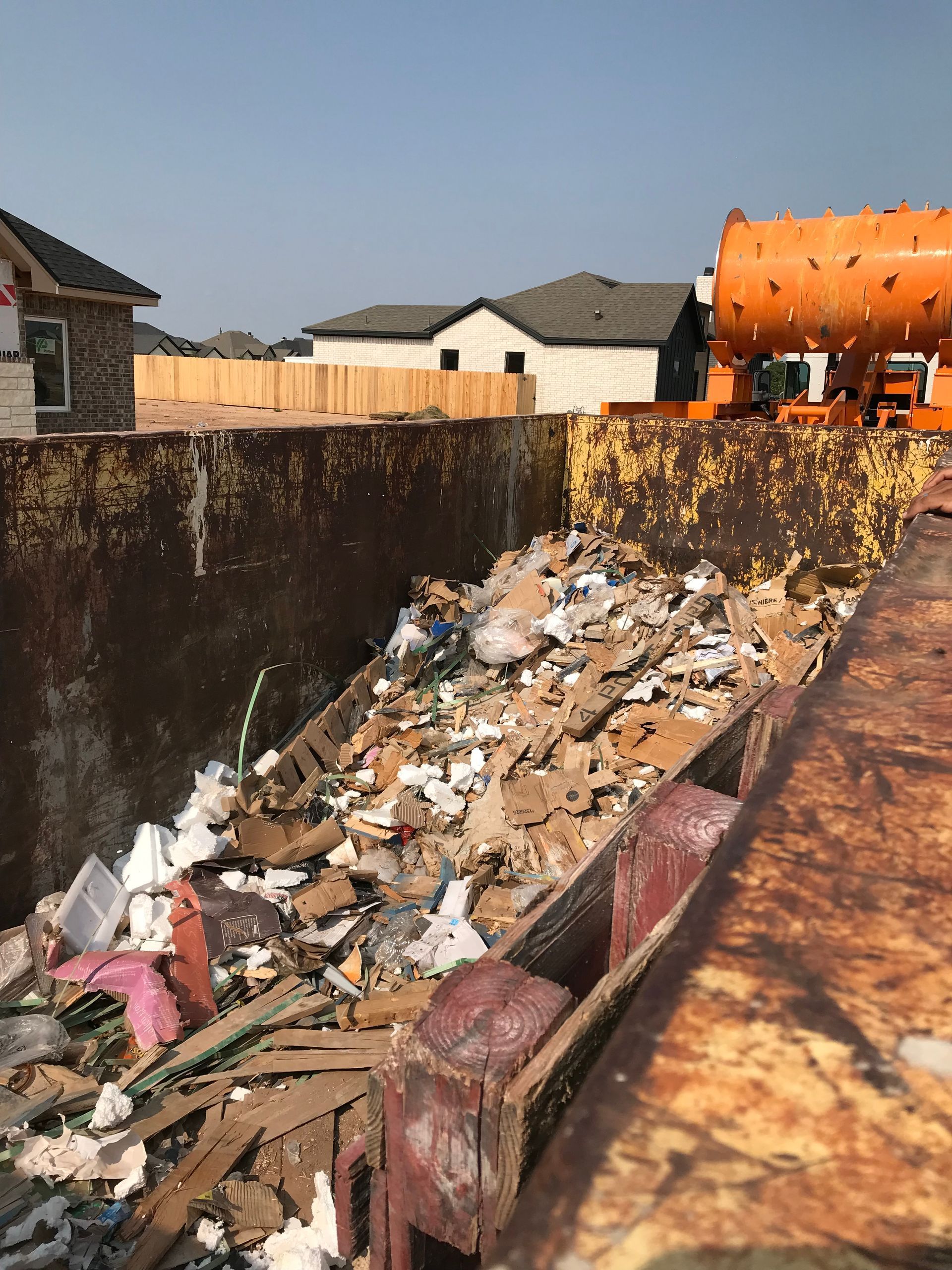 A large industrial dumpster filled with construction debris and cardboard, situated at a residential building site.