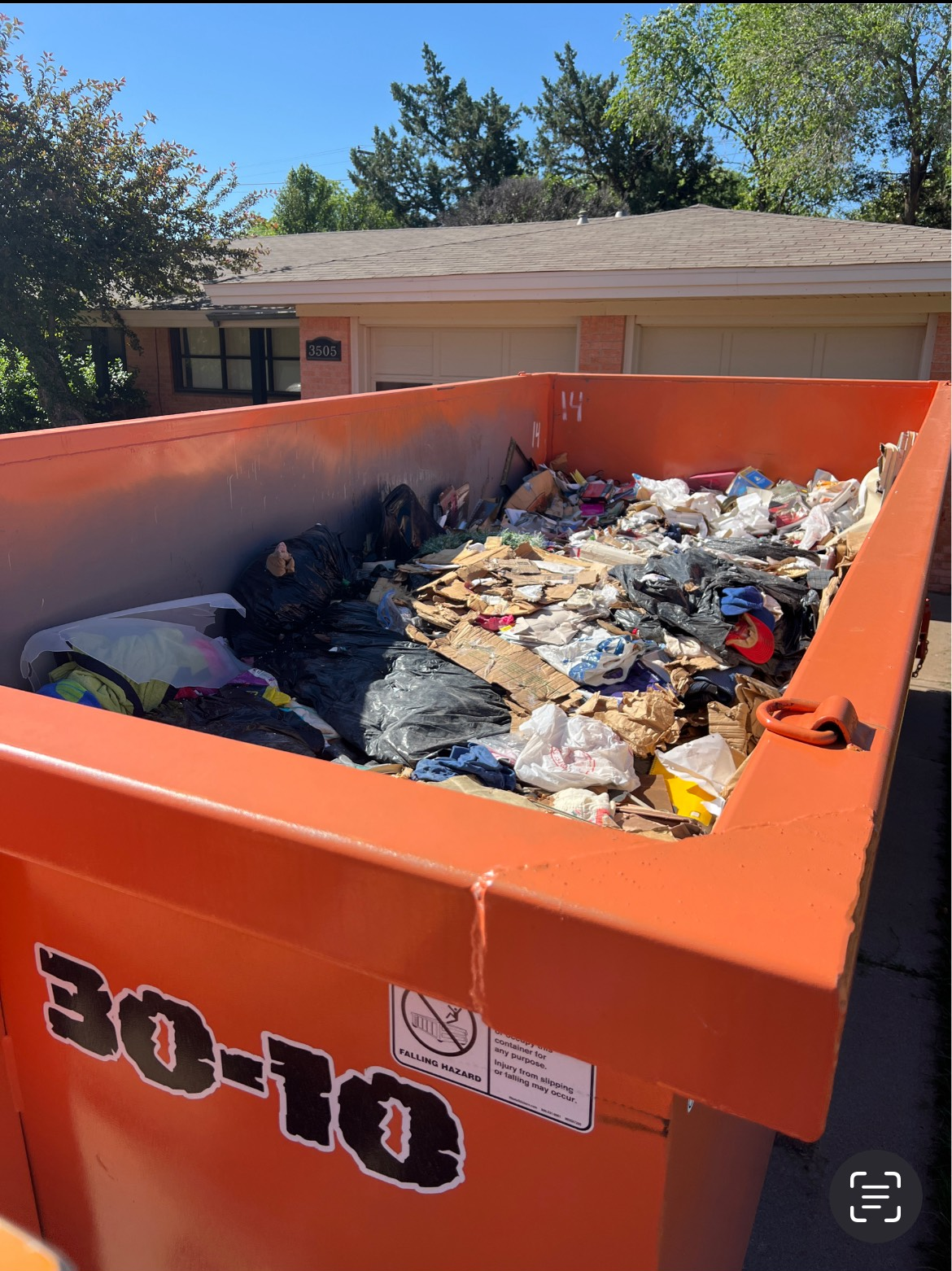 A large industrial dumpster filled with construction debris and cardboard, situated at a residential building site.