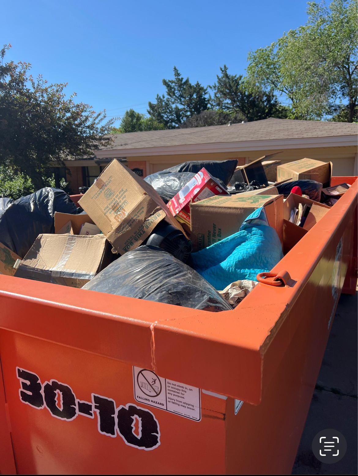 An industrial dumpster filled with scrap wood, pallets, and construction debris at a residential building site.