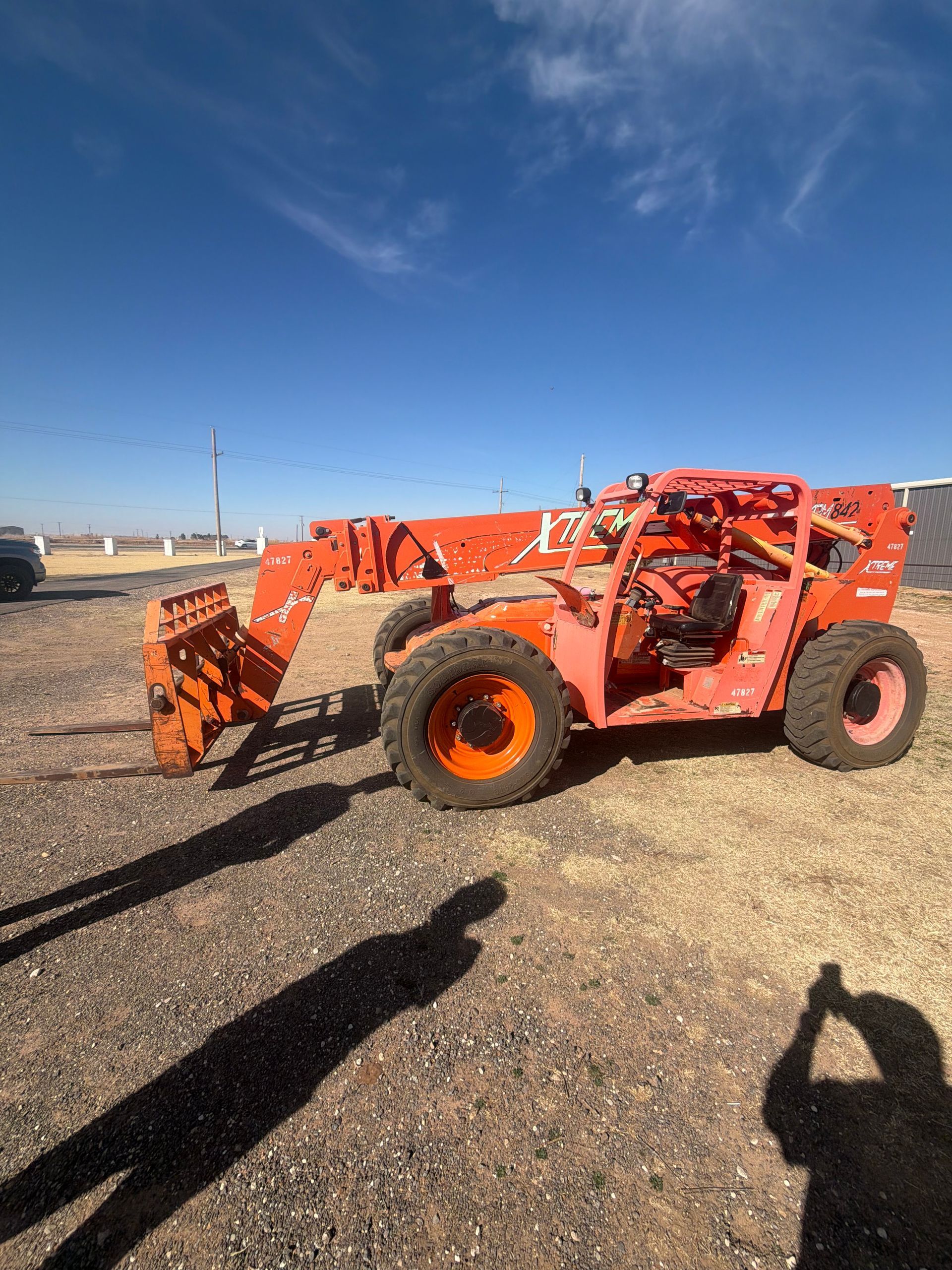 An orange telescopic forklift parked on a gravel lot under a clear blue sky.