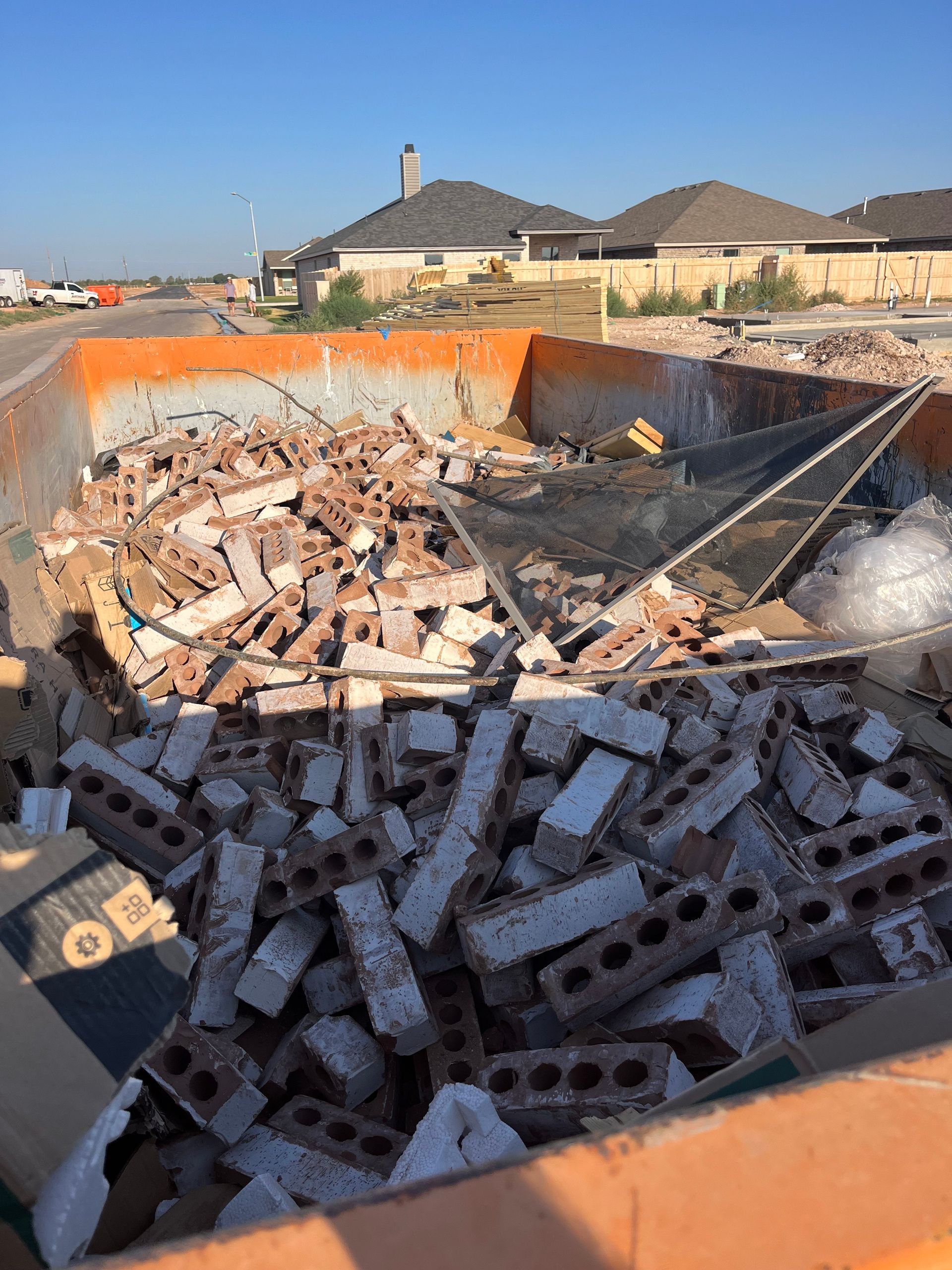 A large orange construction dumpster filled with broken red bricks and debris in a residential building area.