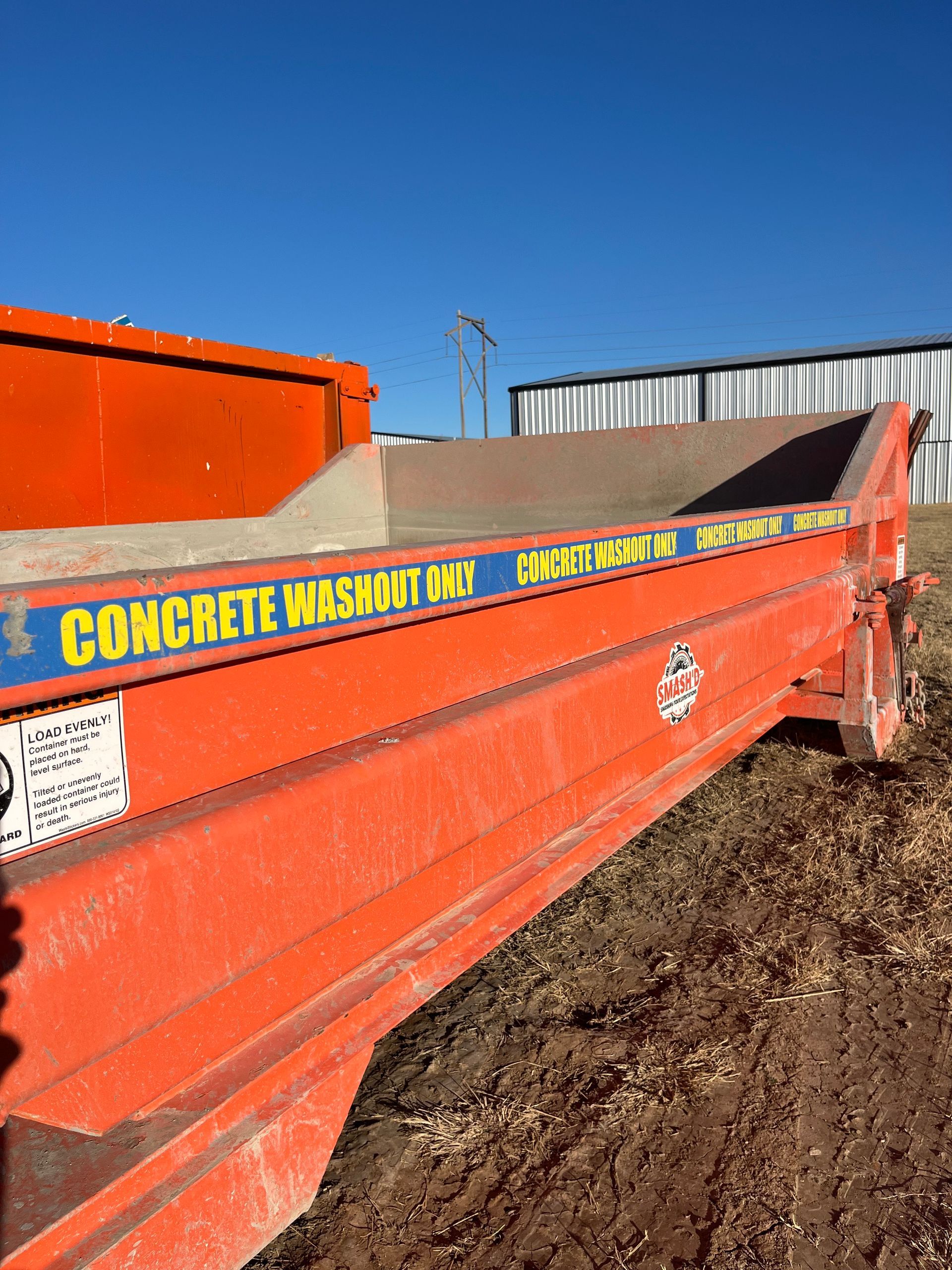 An orange roll-off dumpster sits on dirt, labeled 