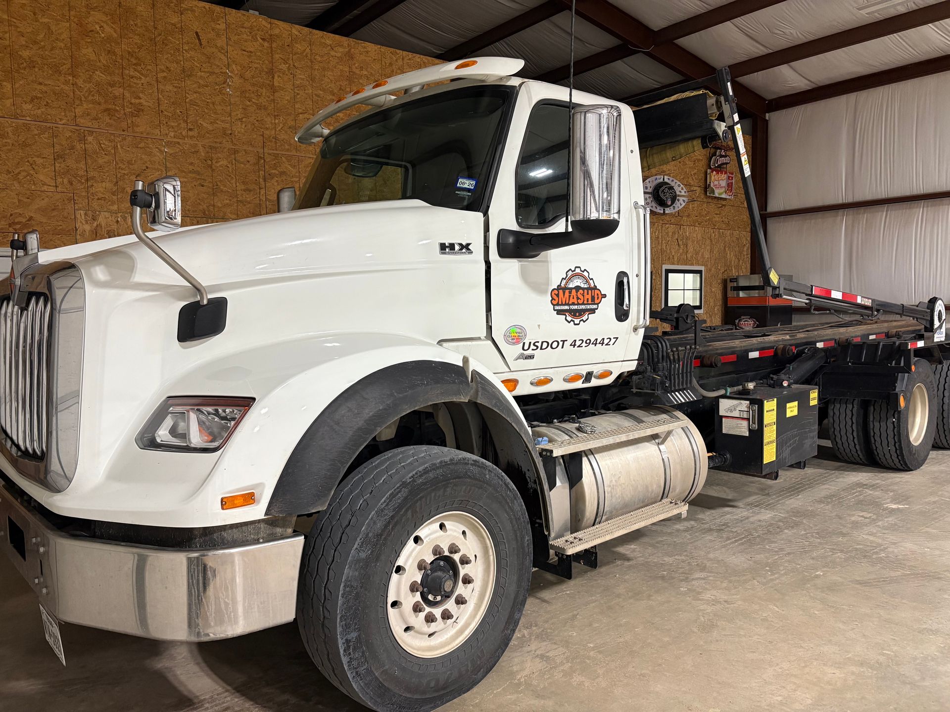 A white roll-off dump truck parked inside a warehouse with wood-paneled walls.